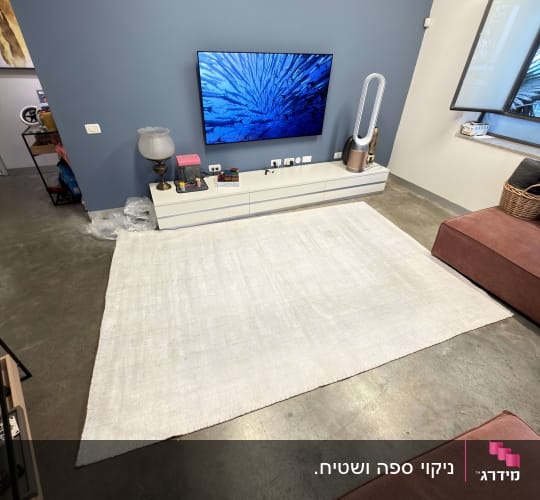 שטיח לבן על רצפת בטון עם טלוויזיה על קיר כחול